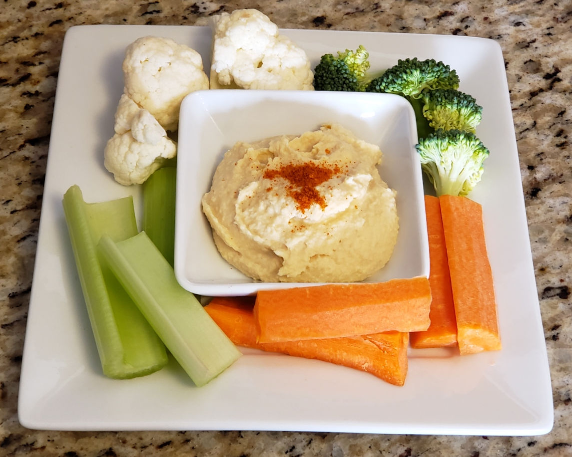 Plate of hummus, topped with paprika and surrounded by vegetables