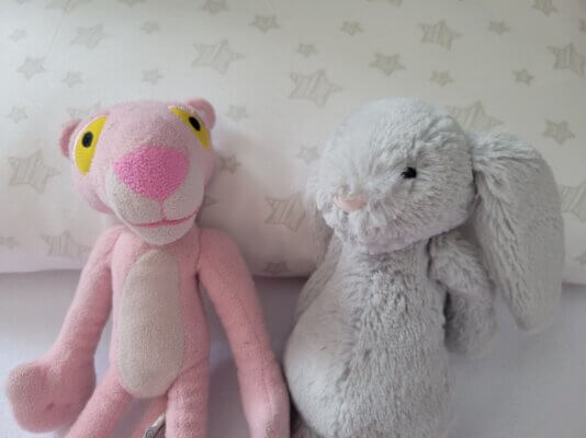 A Pink Panther plush next to a fuzzy rabbit plush, on top of a pillow decorated with stars.